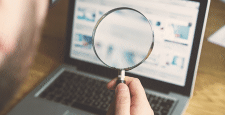 Persoon houdt vergrootglas voor laptopscherm met website, focus op online zoekanalyse