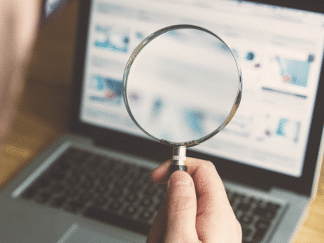 Persoon houdt vergrootglas voor laptopscherm met website, focus op online zoekanalyse